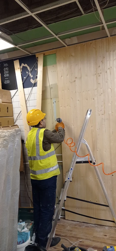 Handyman fixing timber wall cladding to a stud frame with a drill.