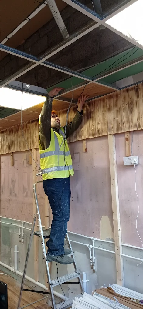 Handyman on a ladder installing a ceiling with LED panels.