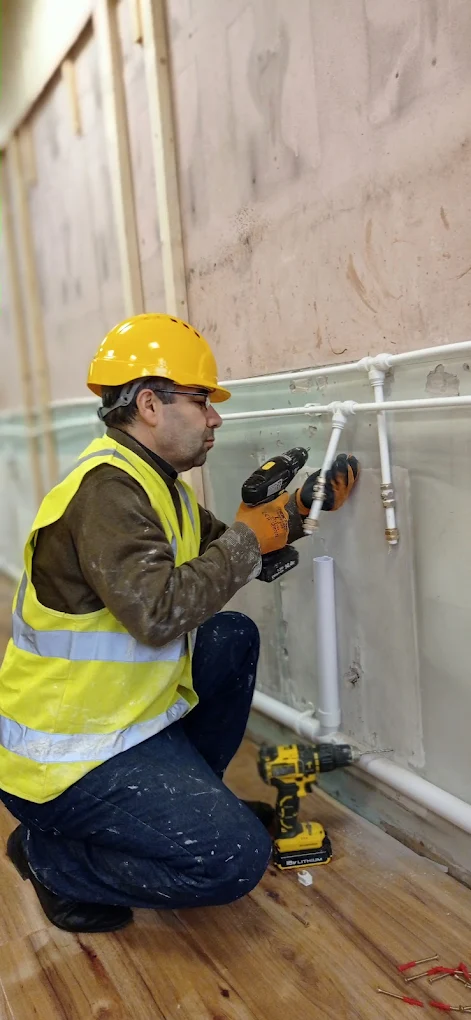 Handyman working next to copper and plastic plumbing pipework.