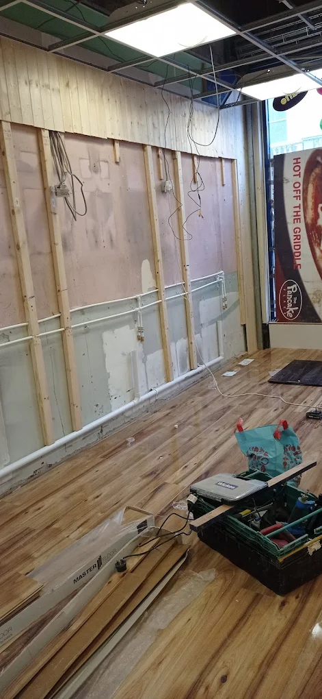 Shop interior mid-refit with exposed studwork, tools and a laid timber floor.