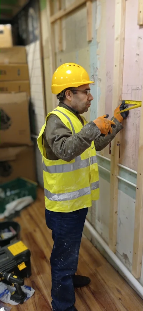 Handyman measuring stud framing against pink plasterboard.