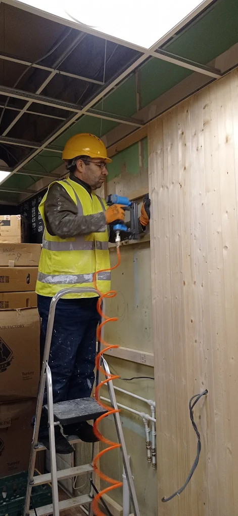Handyman using a pneumatic nailer to fix timber wall panels.